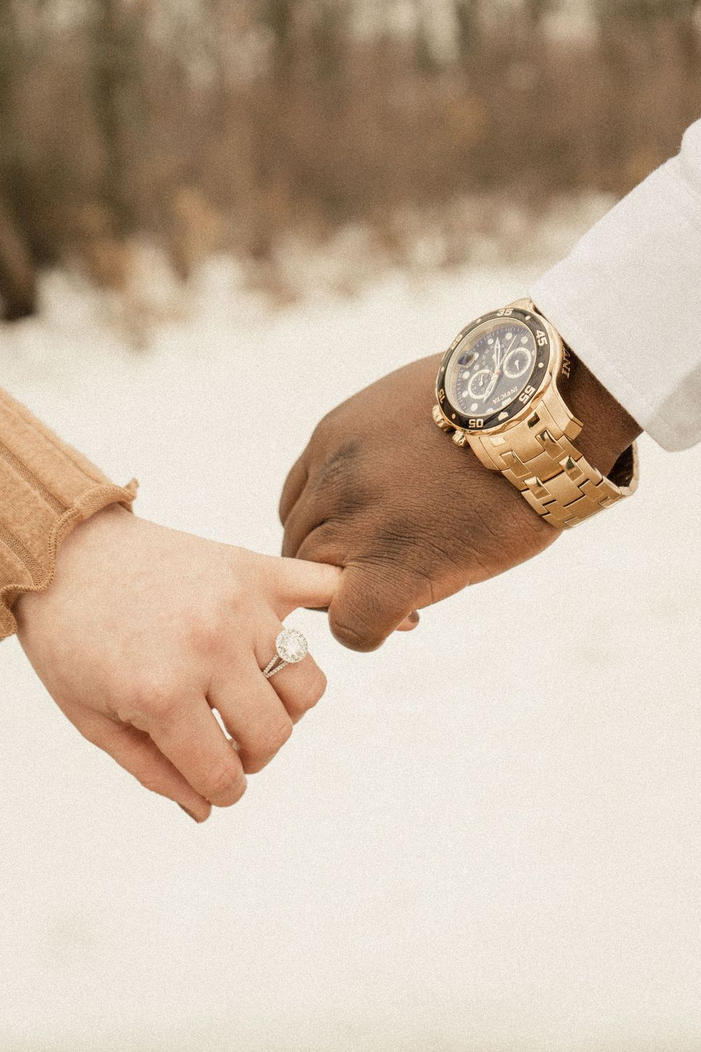 Detail shot of intertwined hands with engagement ring and gold watch against snowy background.
