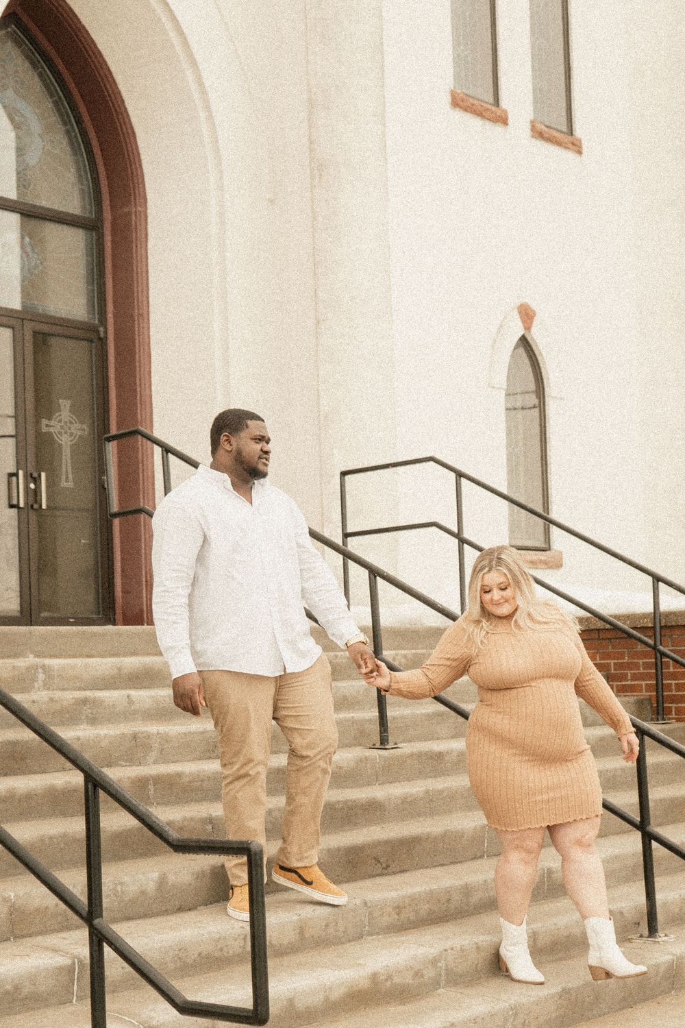 A couple poses on church steps during their engagement photoshoot wearing coordinated outfits.