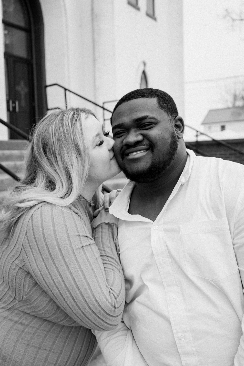 An intimate black and white photo of a couple laughing together outdoors.