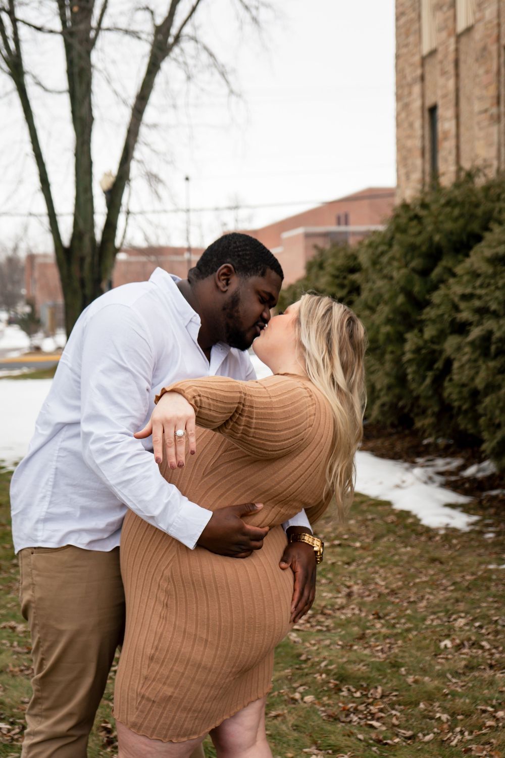 A loving couple embraces in front of a brick building during winter.