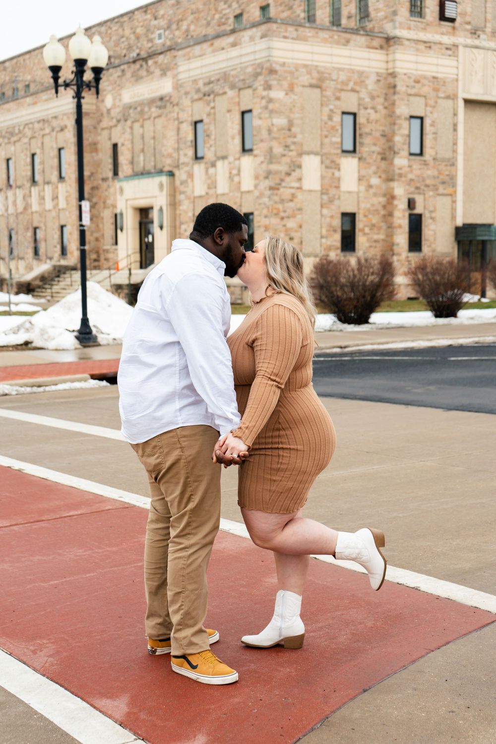 A couple shares a romantic moment on a red crosswalk in front of a historic building.