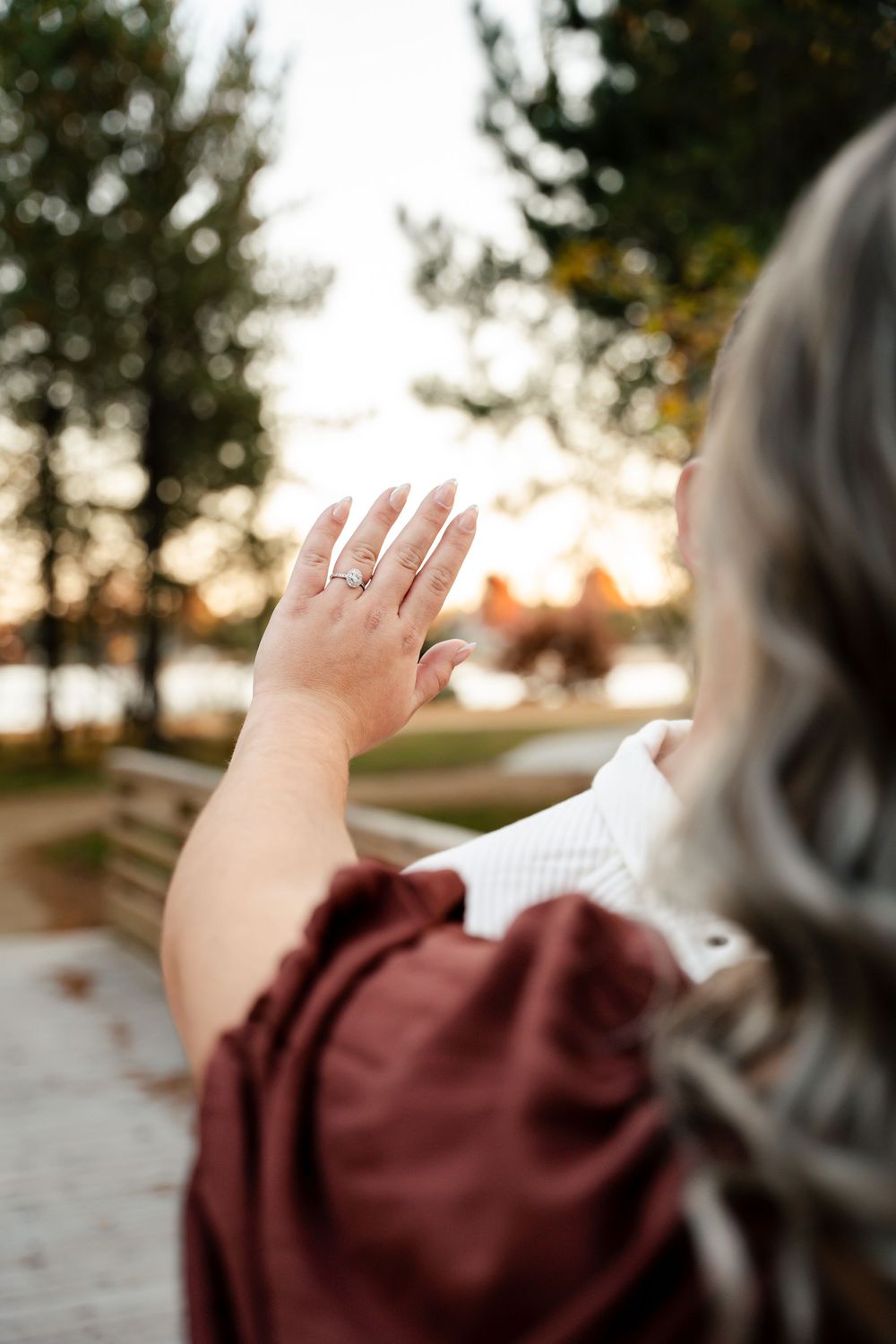 A hand reaches up towards the sky at sunset, wearing a burgundy sleeve against a blurred outdoor background.