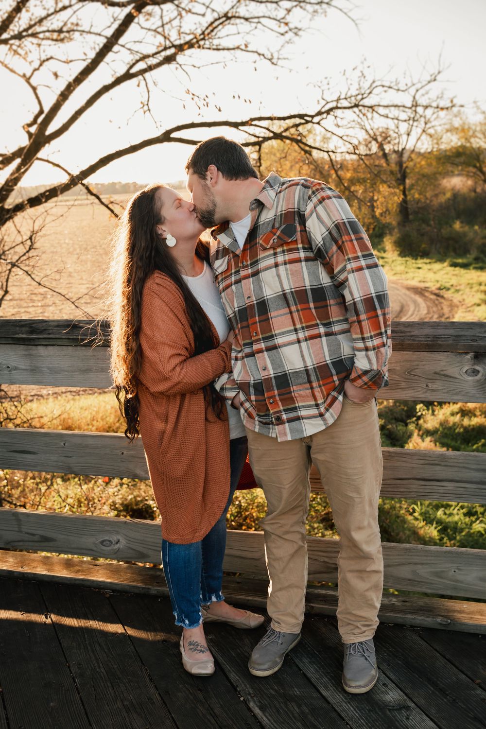 A couple shares a romantic moment on a wooden deck during golden hour at sunset.