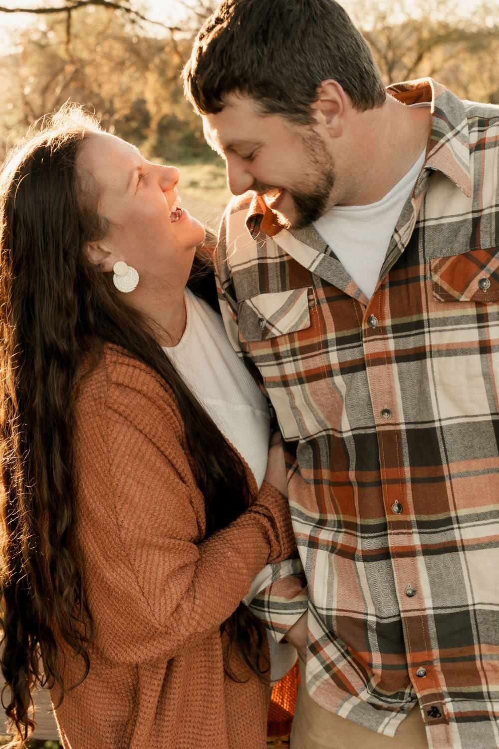 A couple shares a joyful moment together outdoors at sunset wearing autumn-colored clothing.