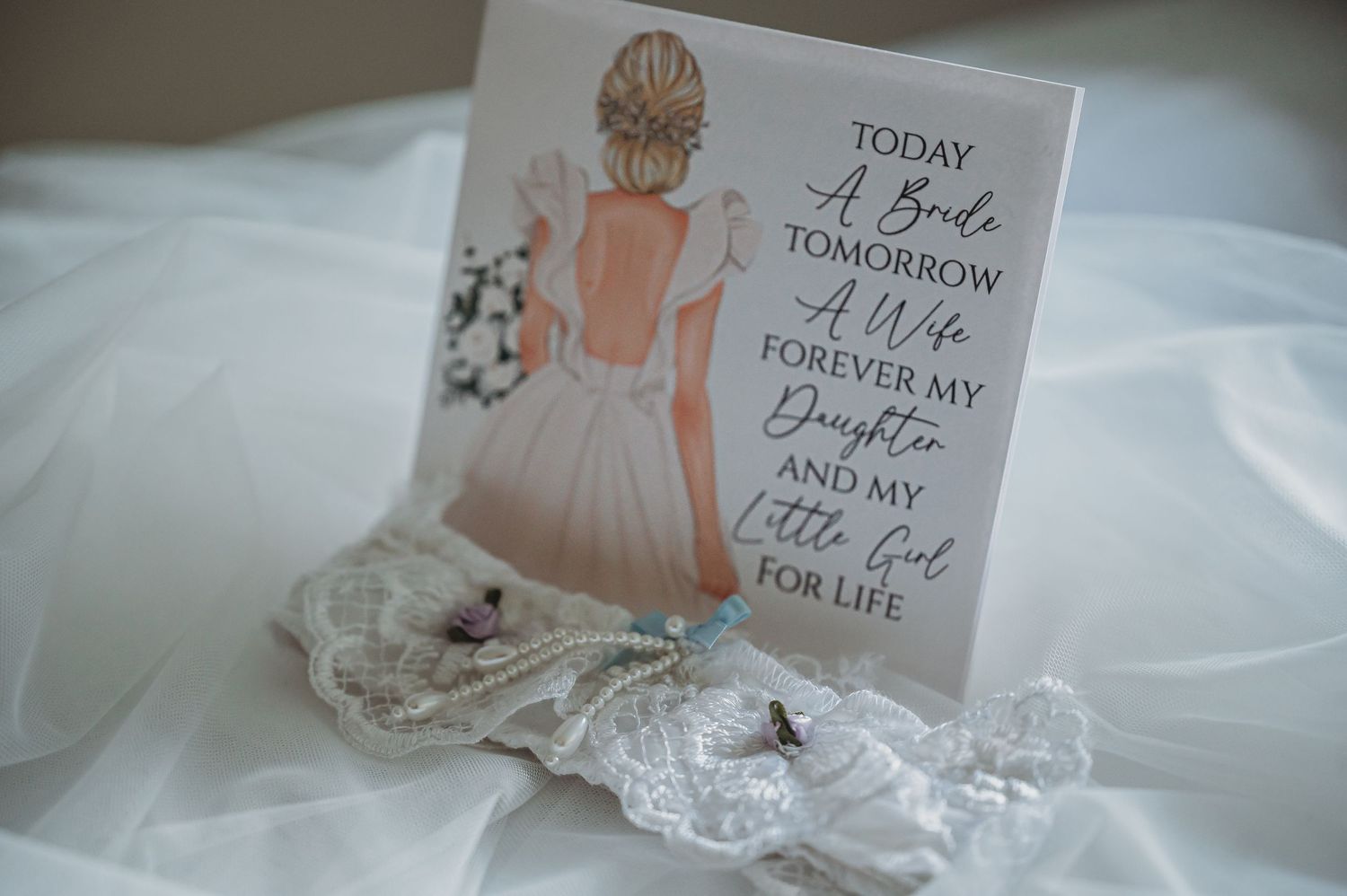 A sentimental wedding card featuring a delicate illustration and text lies beside lace details on white fabric.