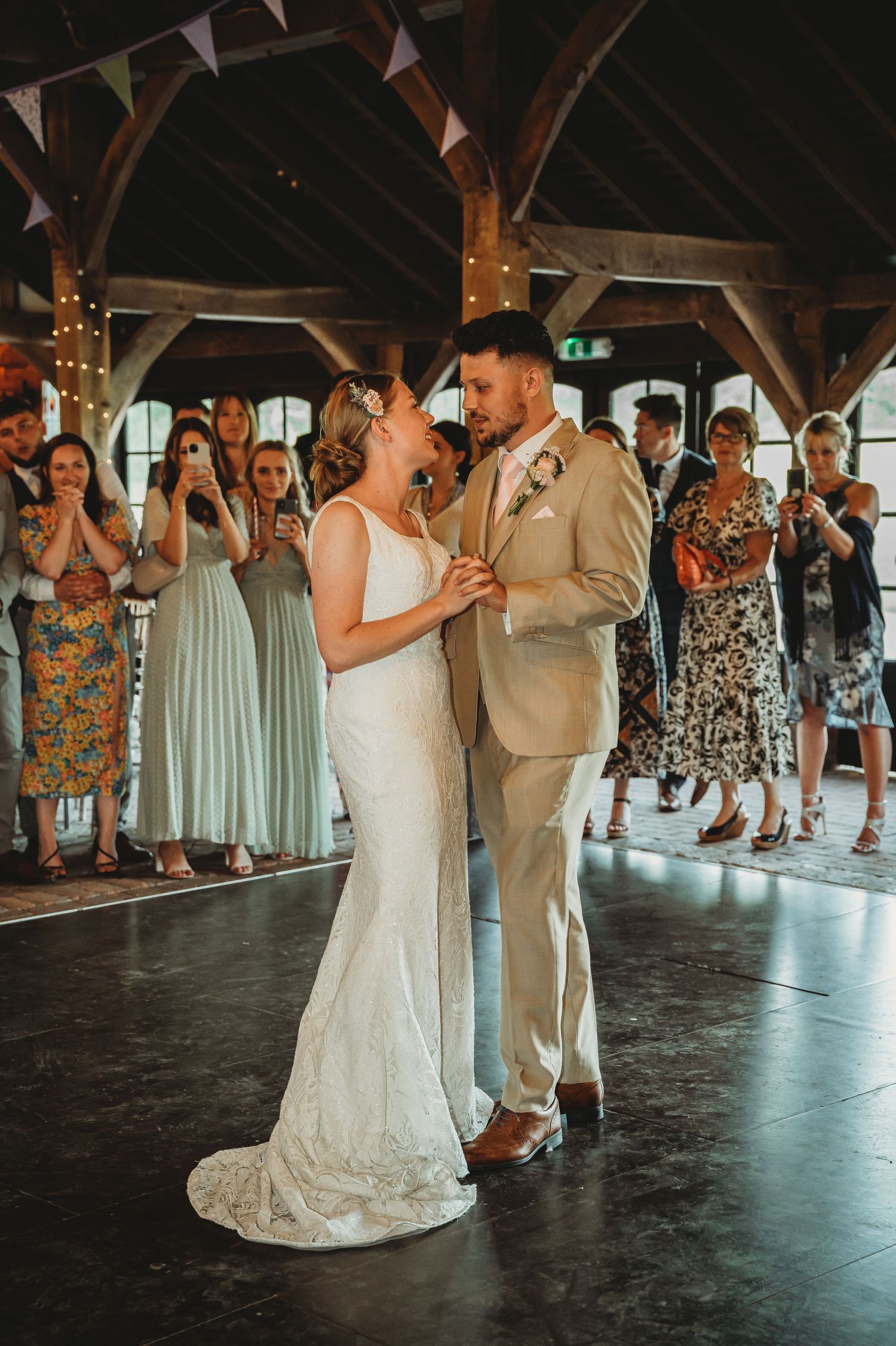 Newlyweds share an intimate moment during their first dance under wooden beams decorated with fairy lights.