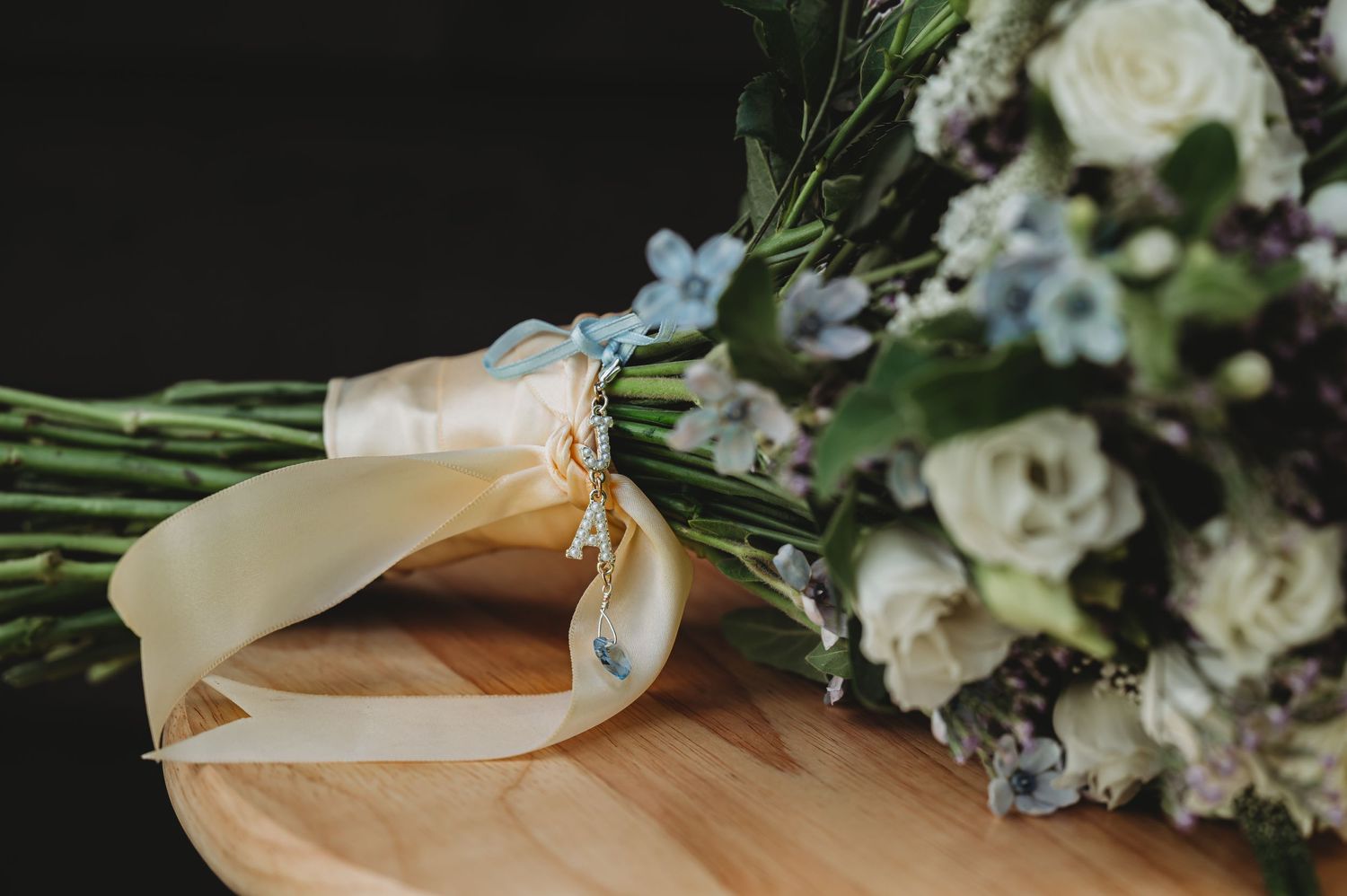 White rose bouquet with delicate blue flowers tied with ribbon rests on wooden surface.