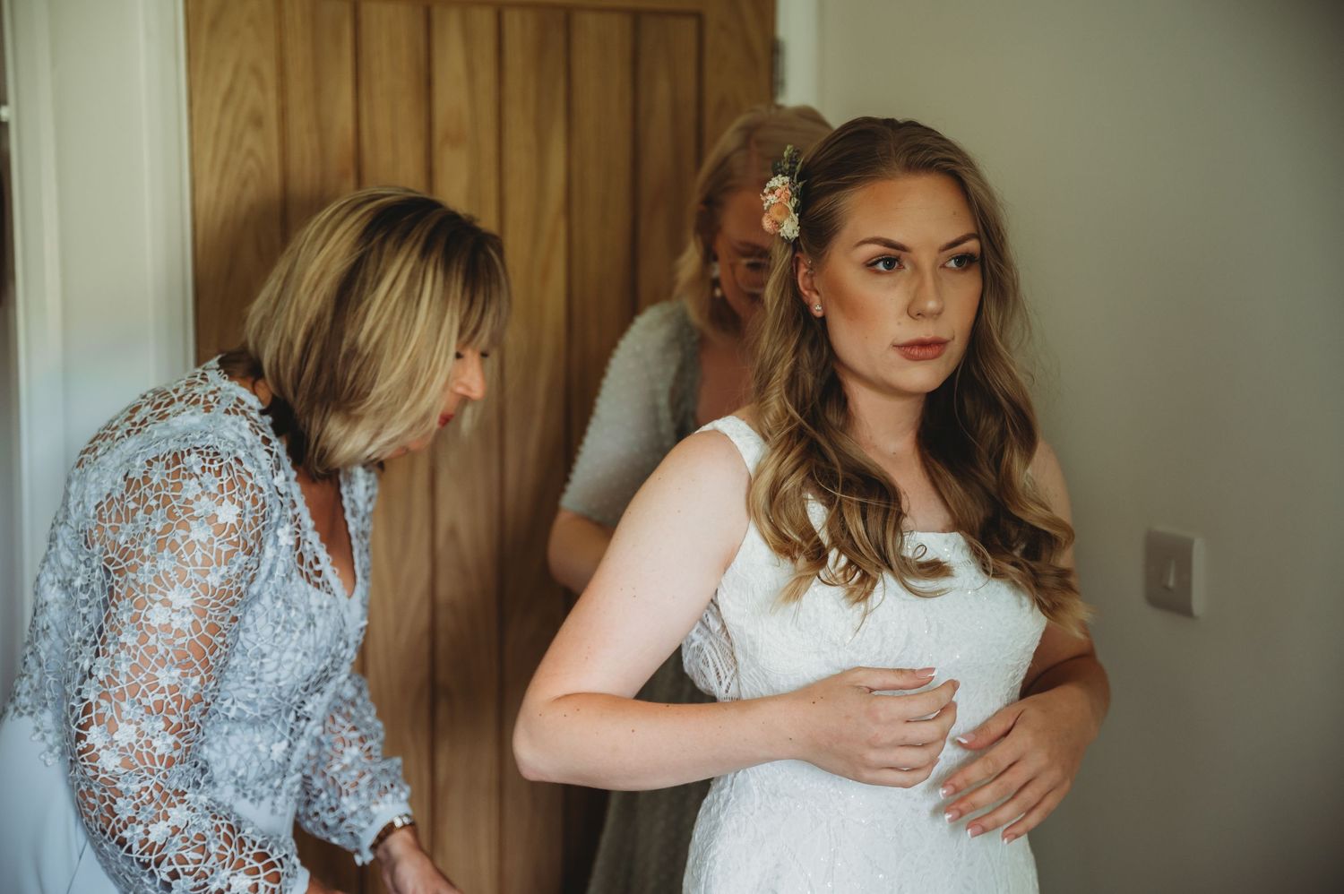 Two people preparing for a wedding ceremony as they get dressed in front of a wooden door with natural lighting.