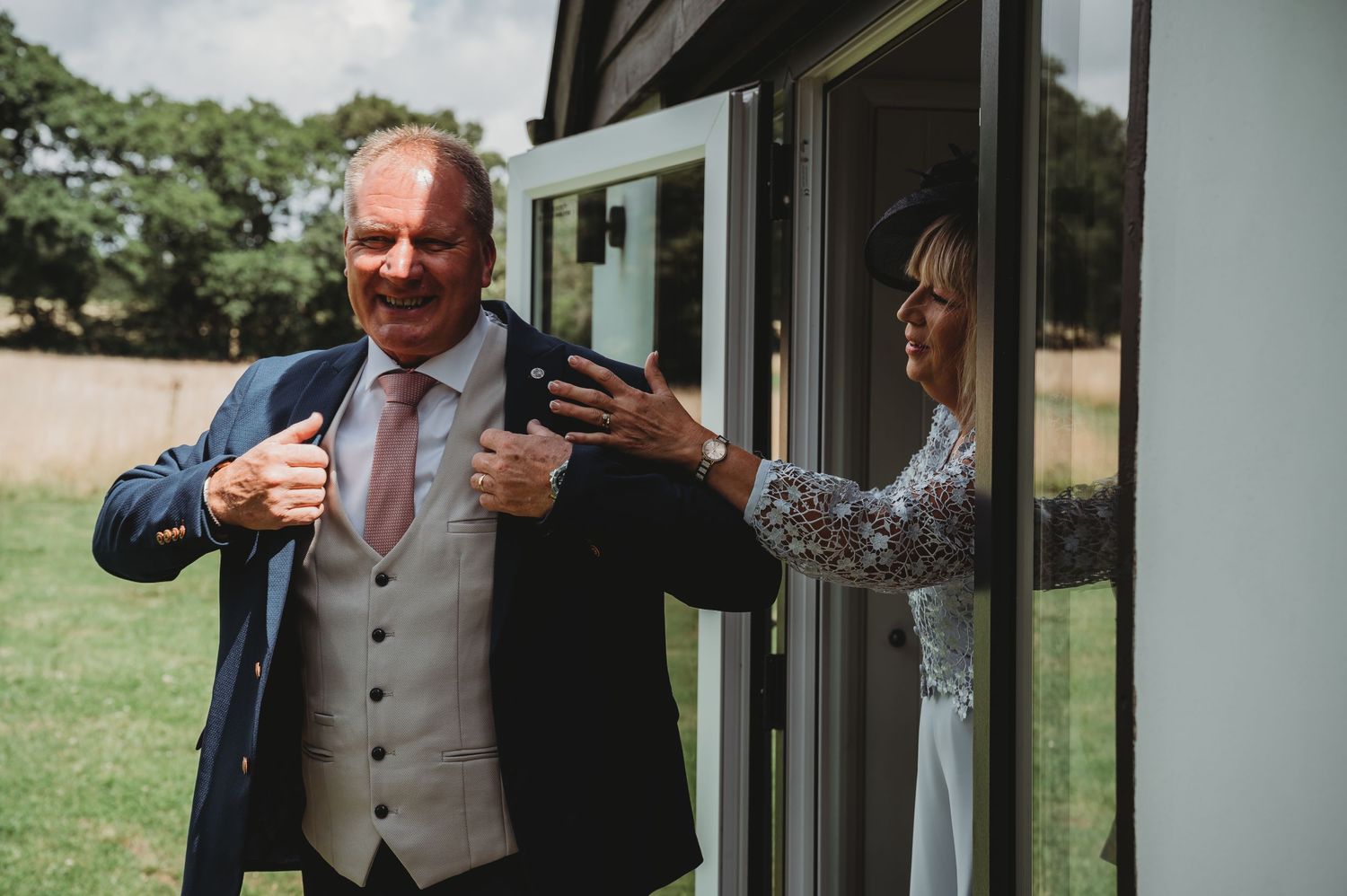 Wedding guests share a candid moment through a glass door at an outdoor venue during a celebration.