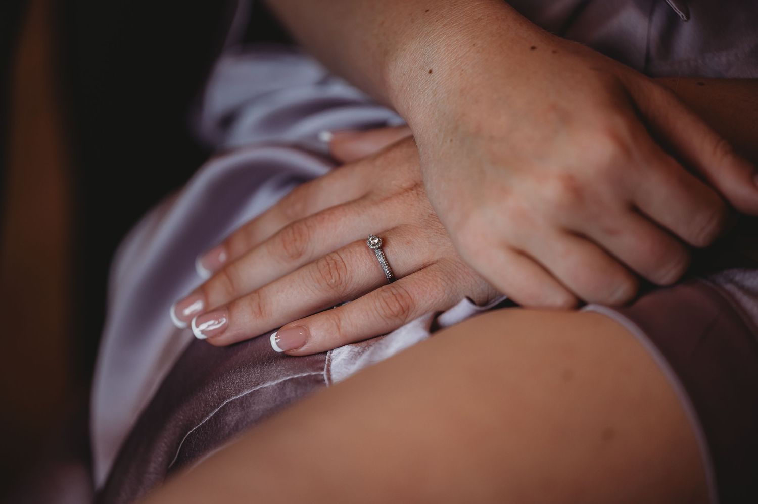 Close up of an engagement ring on someone's hand wearing a silk robe.