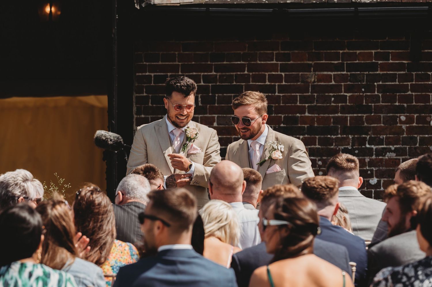 Wedding celebration with guests gathered in front of a brick wall backdrop during an indoor ceremony.