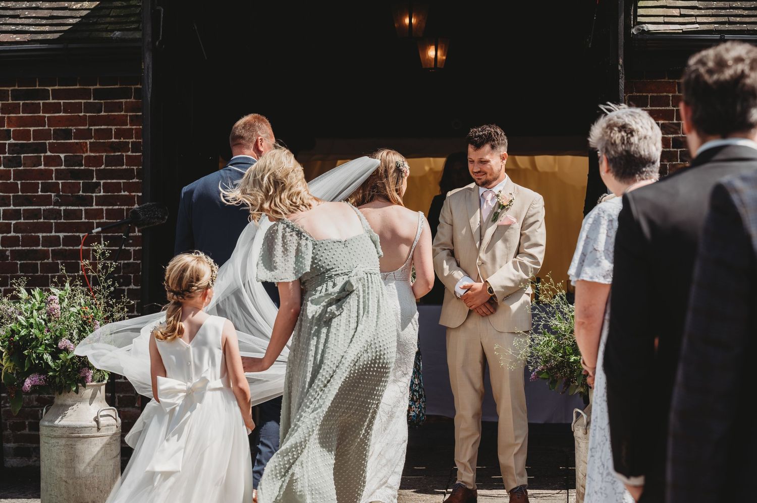 A celebration at a rustic brick-walled venue with guests in formal attire during what appears to be a wedding ceremony.