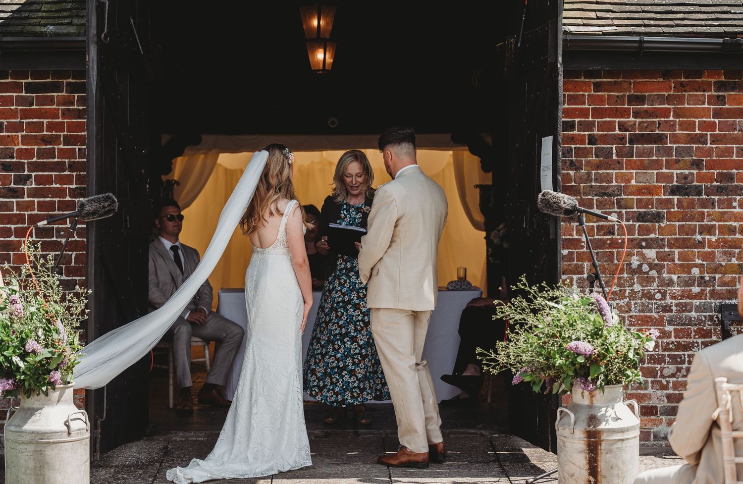 A wedding ceremony takes place in a rustic doorway with exposed brick walls and potted flowers.