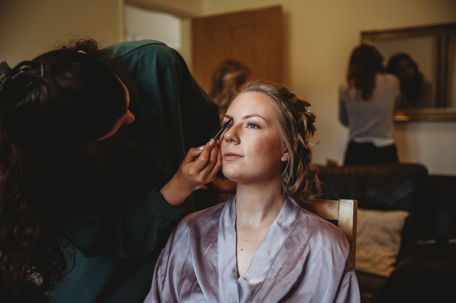 Behind the scenes preparation at a wedding with makeup artist at work in a warm-lit dressing room.