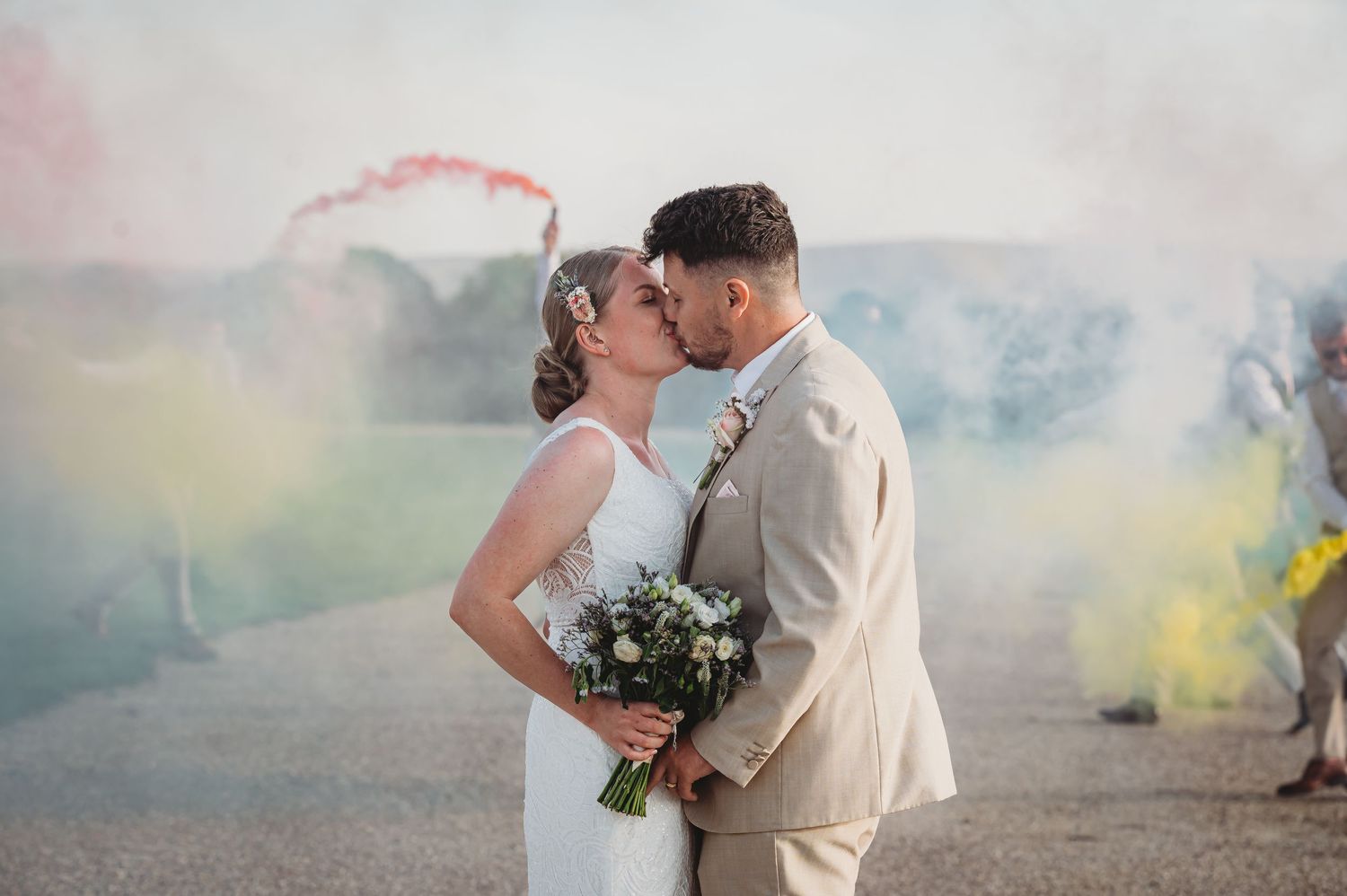 A couple shares their first kiss as newlyweds surrounded by colorful smoke flares.