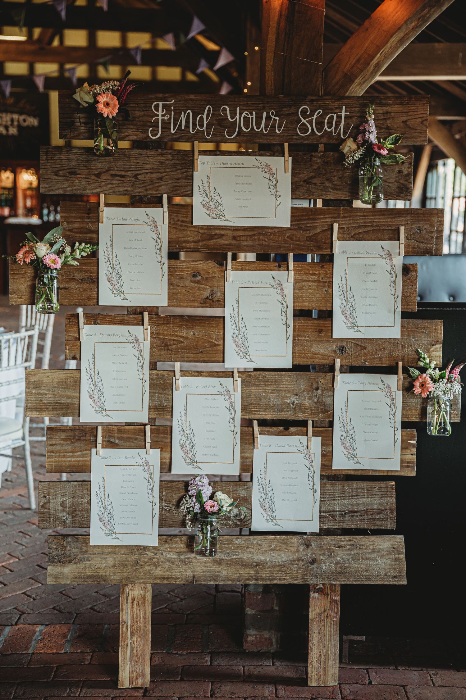 Rustic wooden seating chart display with white frames and pink floral arrangements for a barn wedding reception.