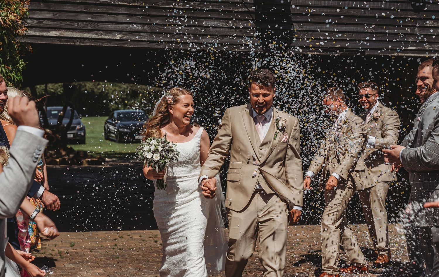 Wedding couple and party joyfully walk through shower of confetti outside on sunny day.