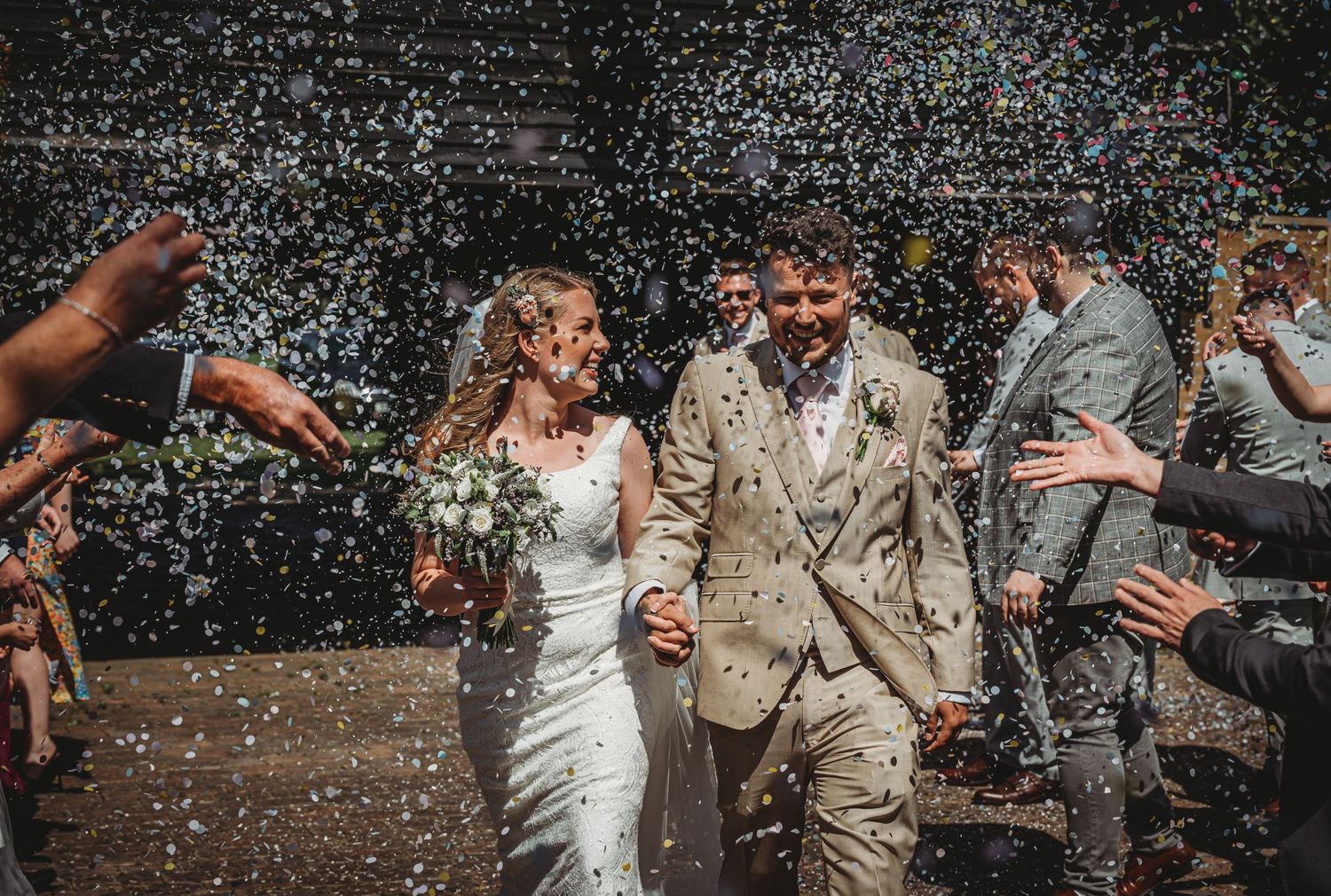 Newlywed couple walking through a shower of confetti while wedding guests celebrate their joyous moment.