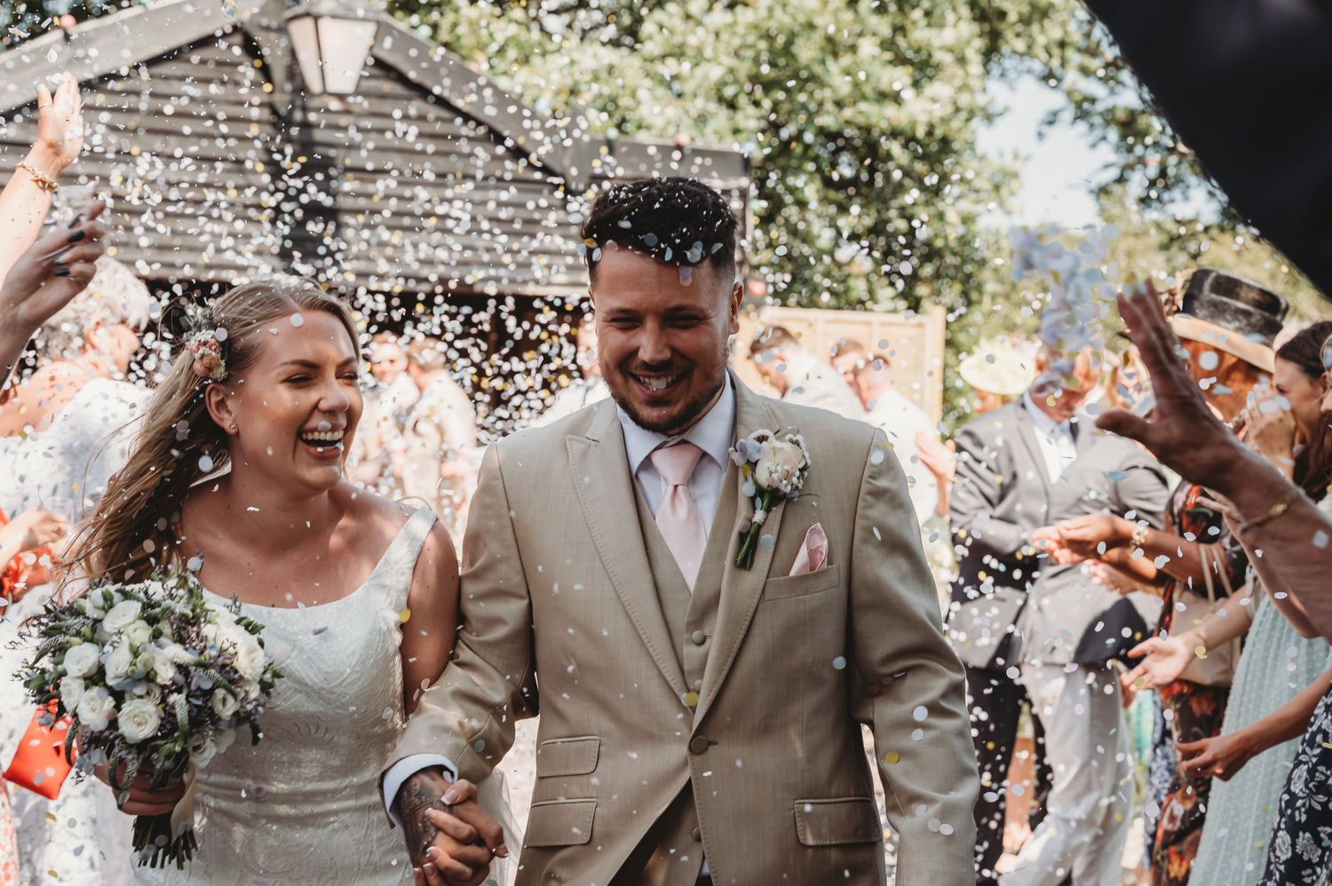 A joyous wedding celebration with confetti being thrown as the newlyweds walk down the aisle in outdoor ceremony.