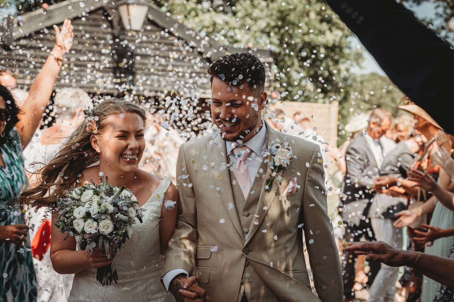Wedding celebration outdoors with confetti being thrown over couple in joyous moment during ceremony.