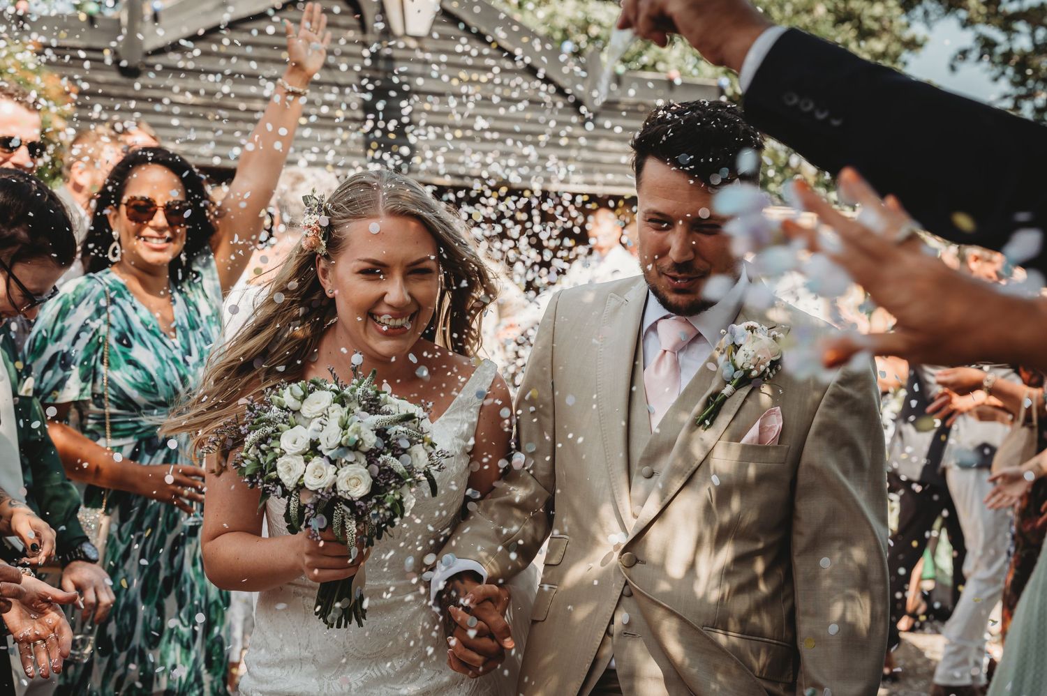 Wedding celebration with guests tossing flower petals over a newlywed couple during outdoor ceremony exit.