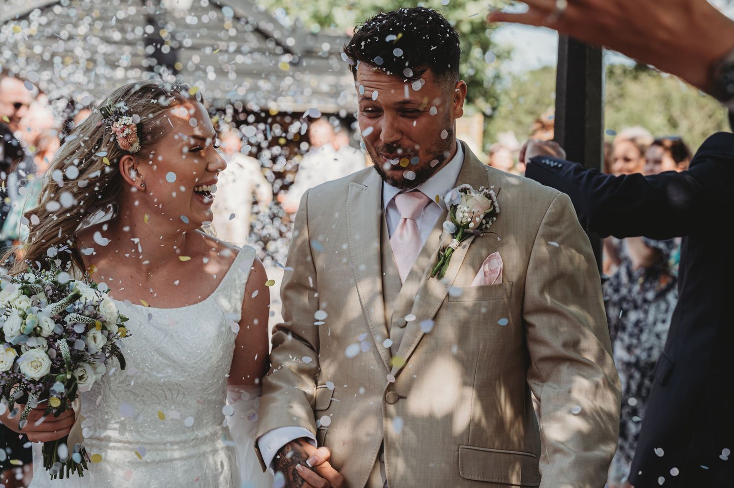 Joyful newlyweds walk through a shower of confetti at an outdoor wedding ceremony in summer.
