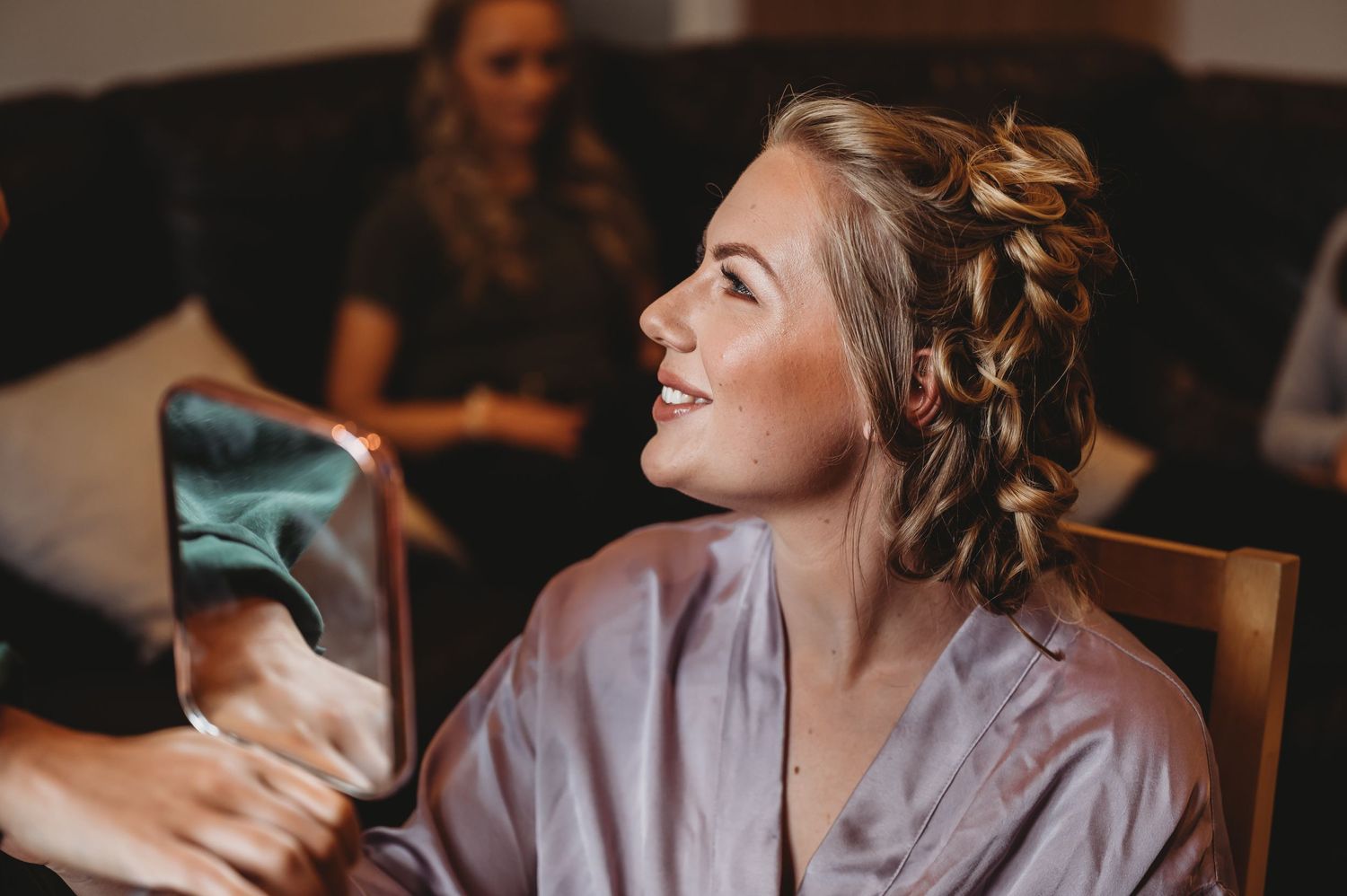 A bride in a silk robe smiles while getting ready in the morning during wedding preparations.