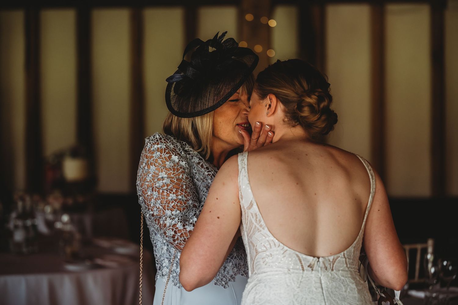 Two people in wedding dresses share an intimate moment at an indoor reception venue.