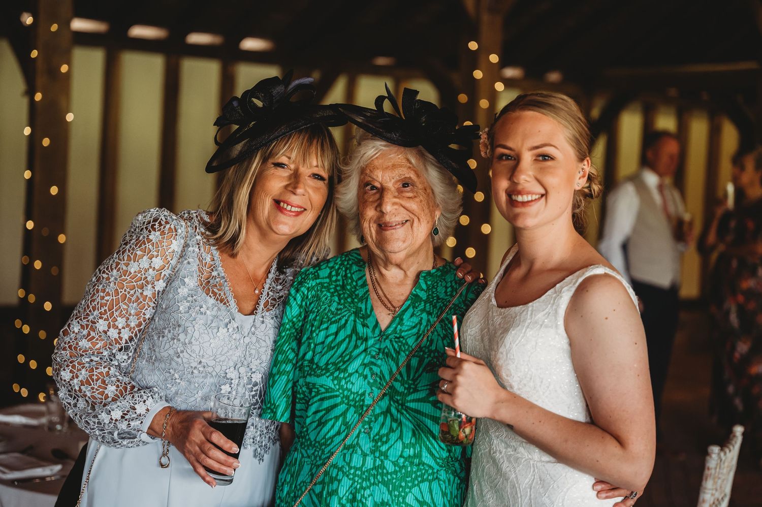 Three generations gather at a festive event wearing elegant dresses in silver, emerald green and white.