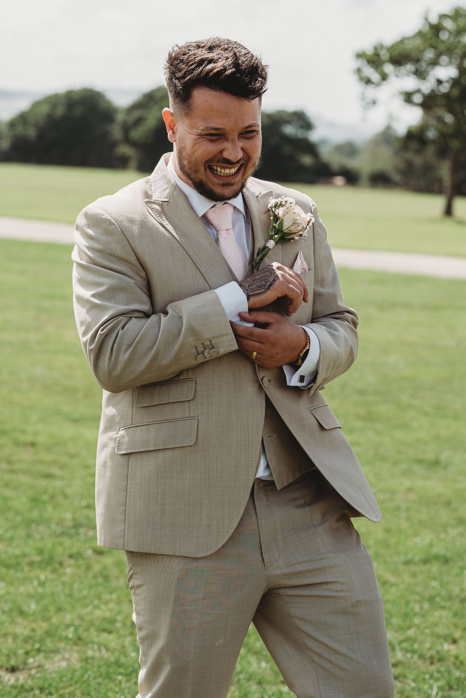 A joyful wedding moment captured outdoors showing someone in a light beige suit laughing while checking their phone.