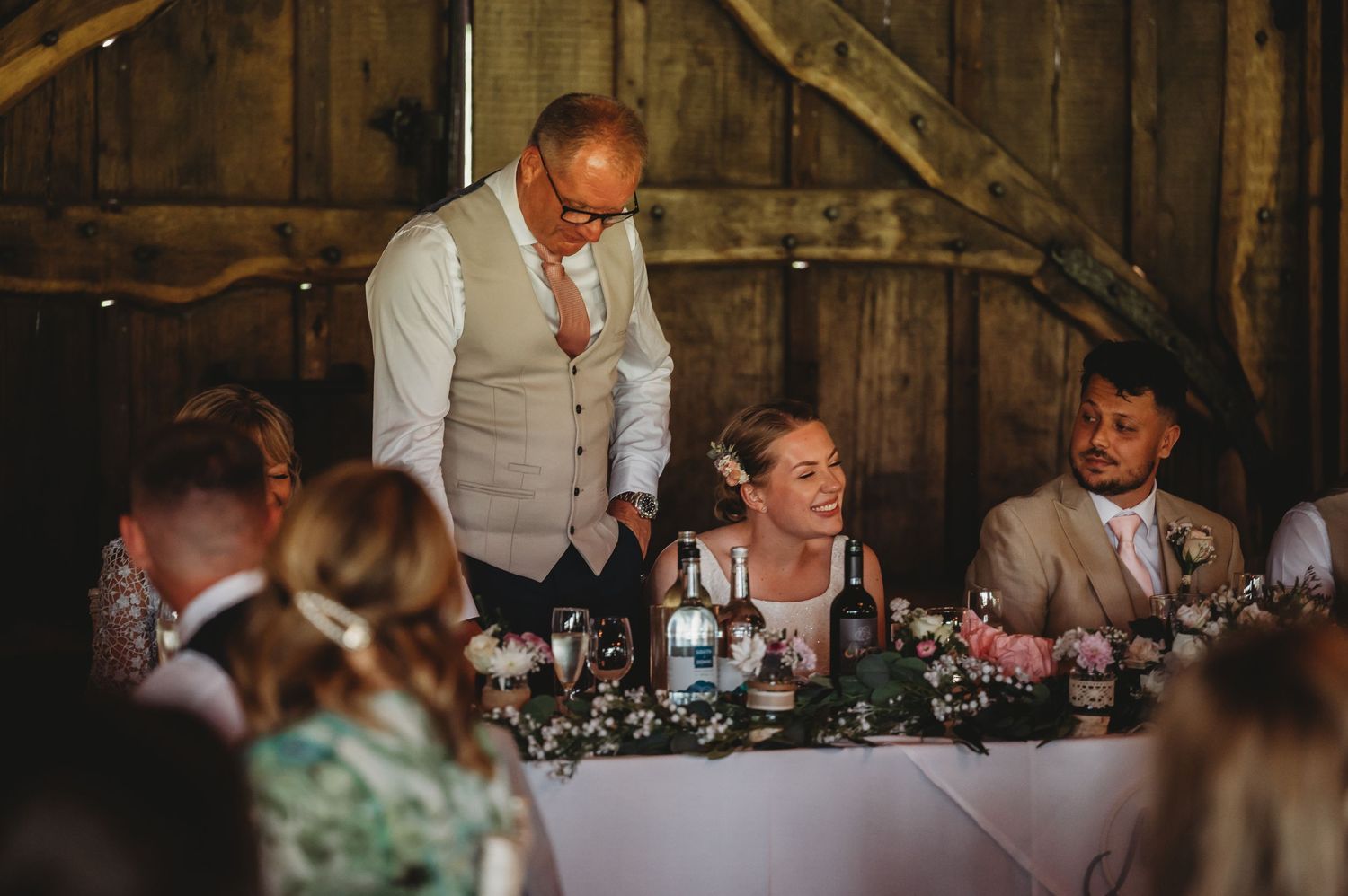 Wedding guests seated at a rustic barn reception with elegant table decorations and floral centerpieces.