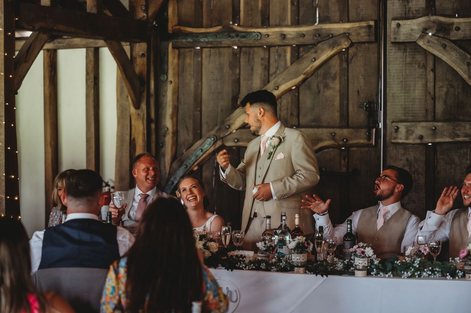 Wedding reception toast inside a rustic barn setting with decorated head table and guests gathered during celebration.