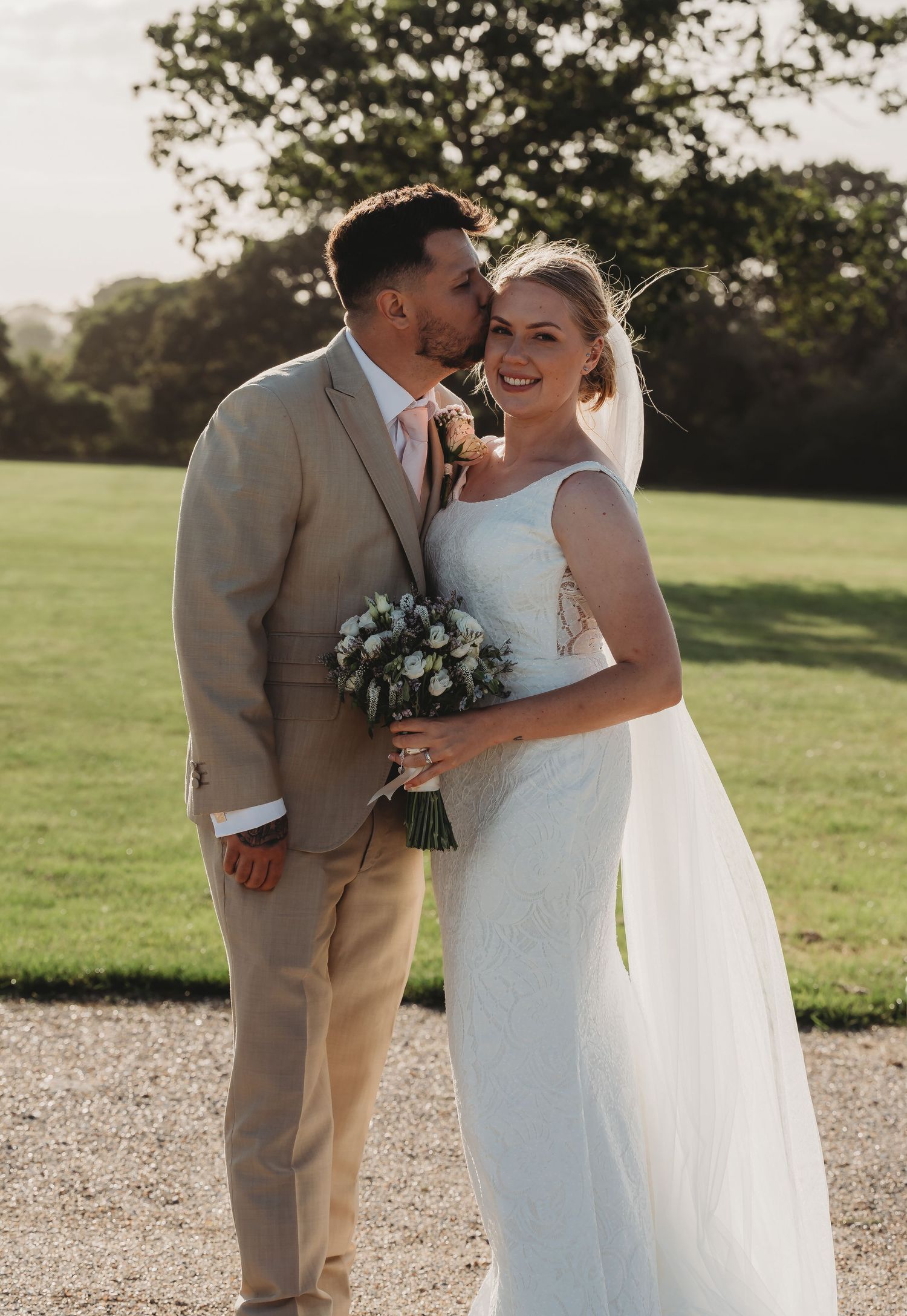 A couple shares an intimate moment during their outdoor wedding ceremony in golden sunlight on a grassy lawn.
