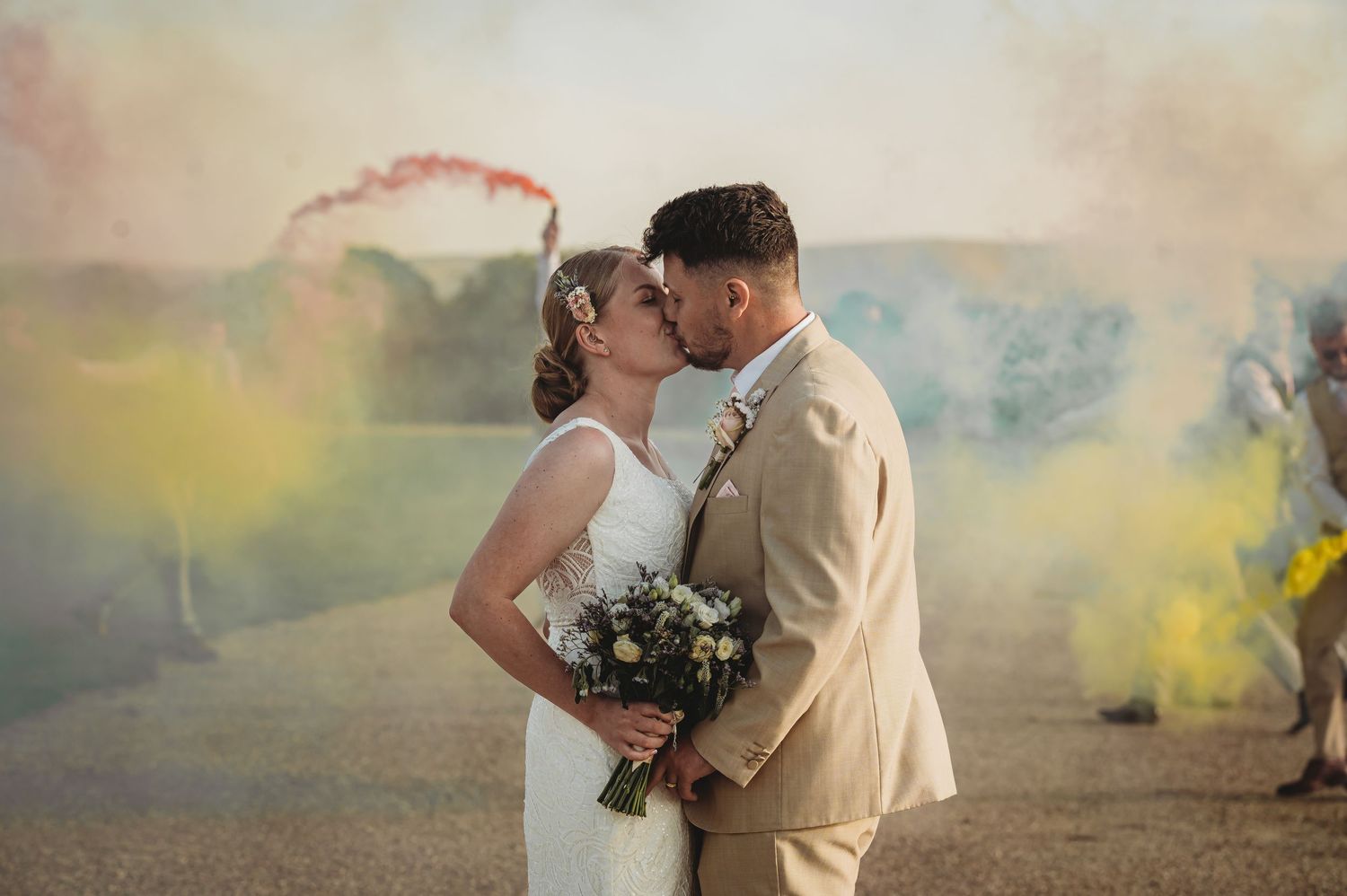 A romantic wedding couple shares a tender moment embracing in colorful smoke during an outdoor ceremony.