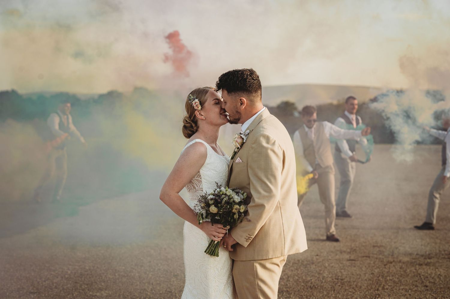 A couple sharing an intimate moment surrounded by colorful smoke during their outdoor wedding celebration.