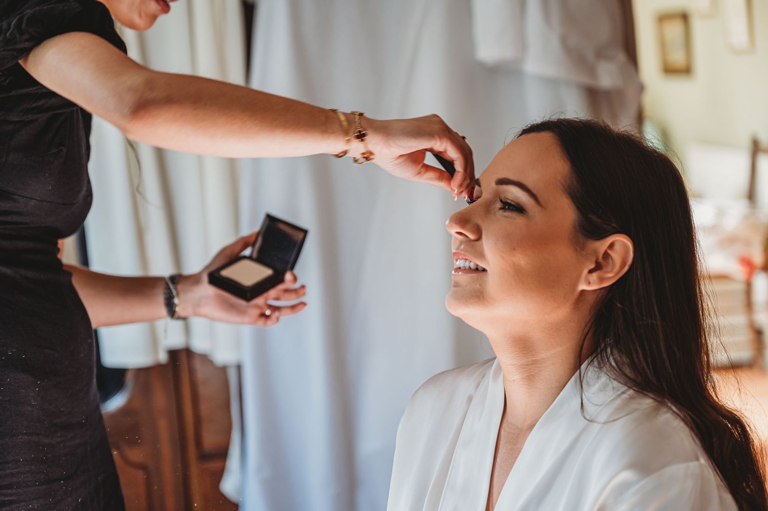 Makeup artist applies cosmetics to the client's face during beauty appointment in a bright room.