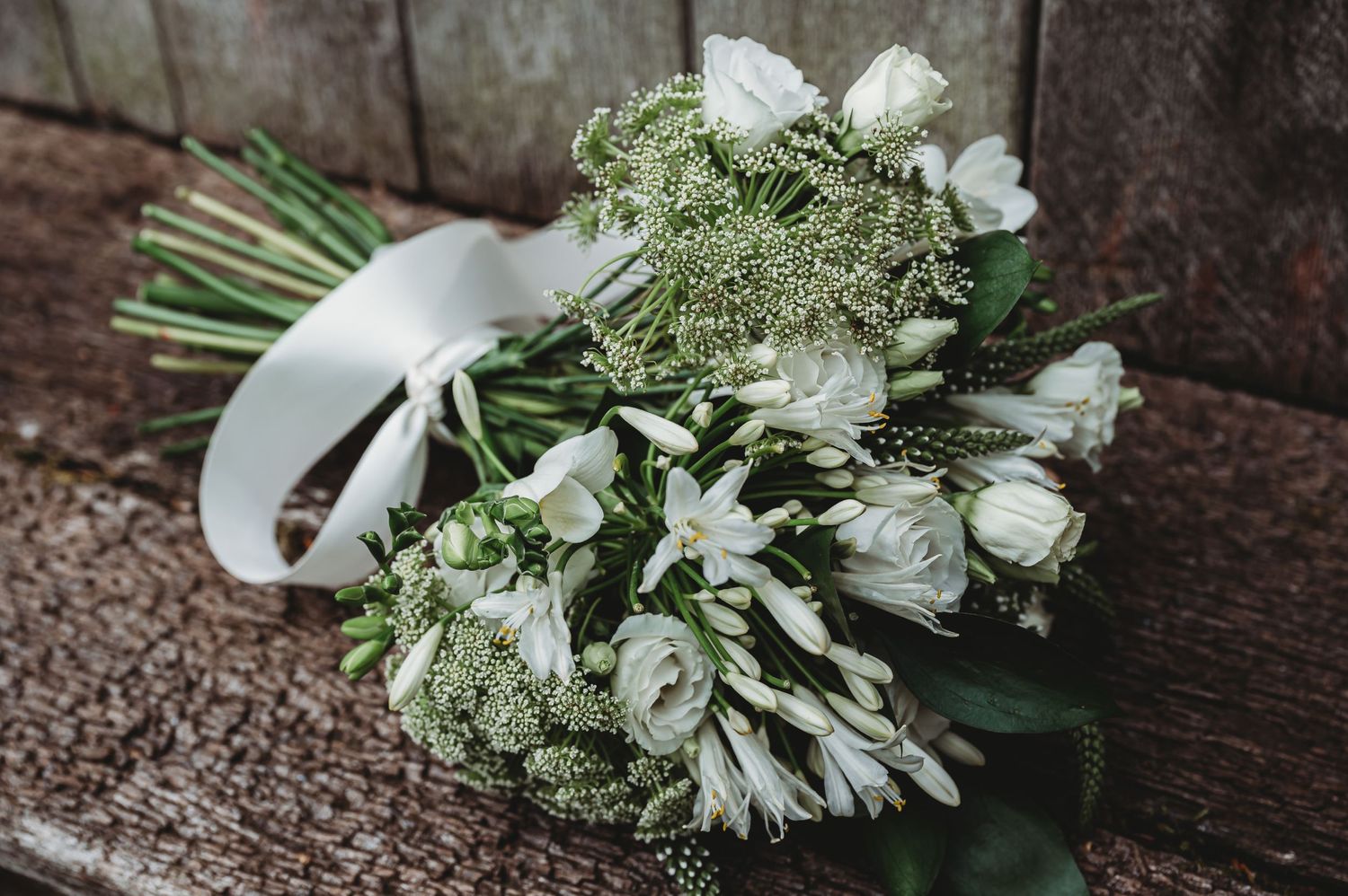 A fresh bridal bouquet featuring white flowers, Queen Anne's lace, and greenery arranged on a rustic wooden surface.