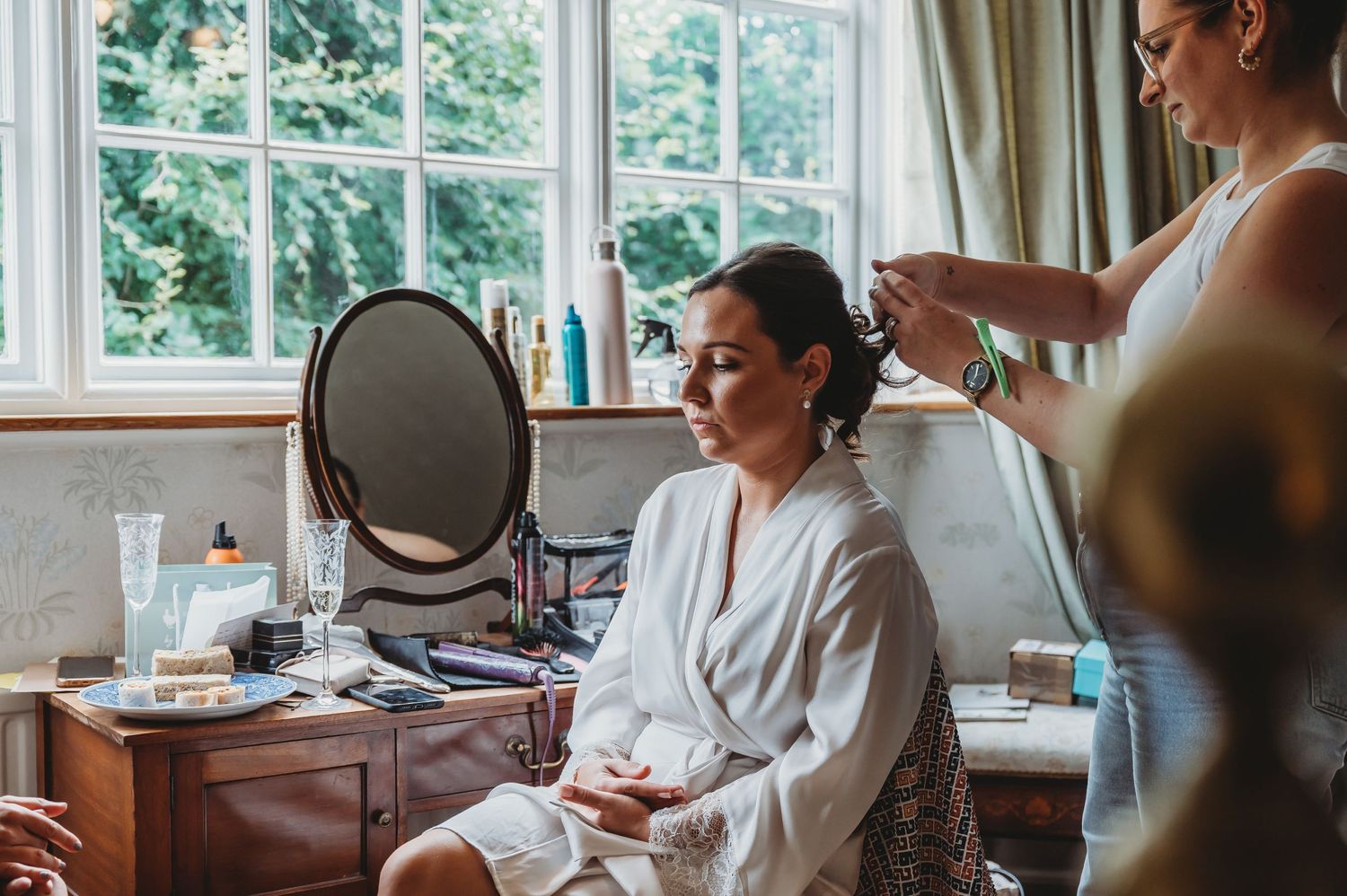 Getting ready in a bright room with natural light from windows while having hair styled in a white robe.