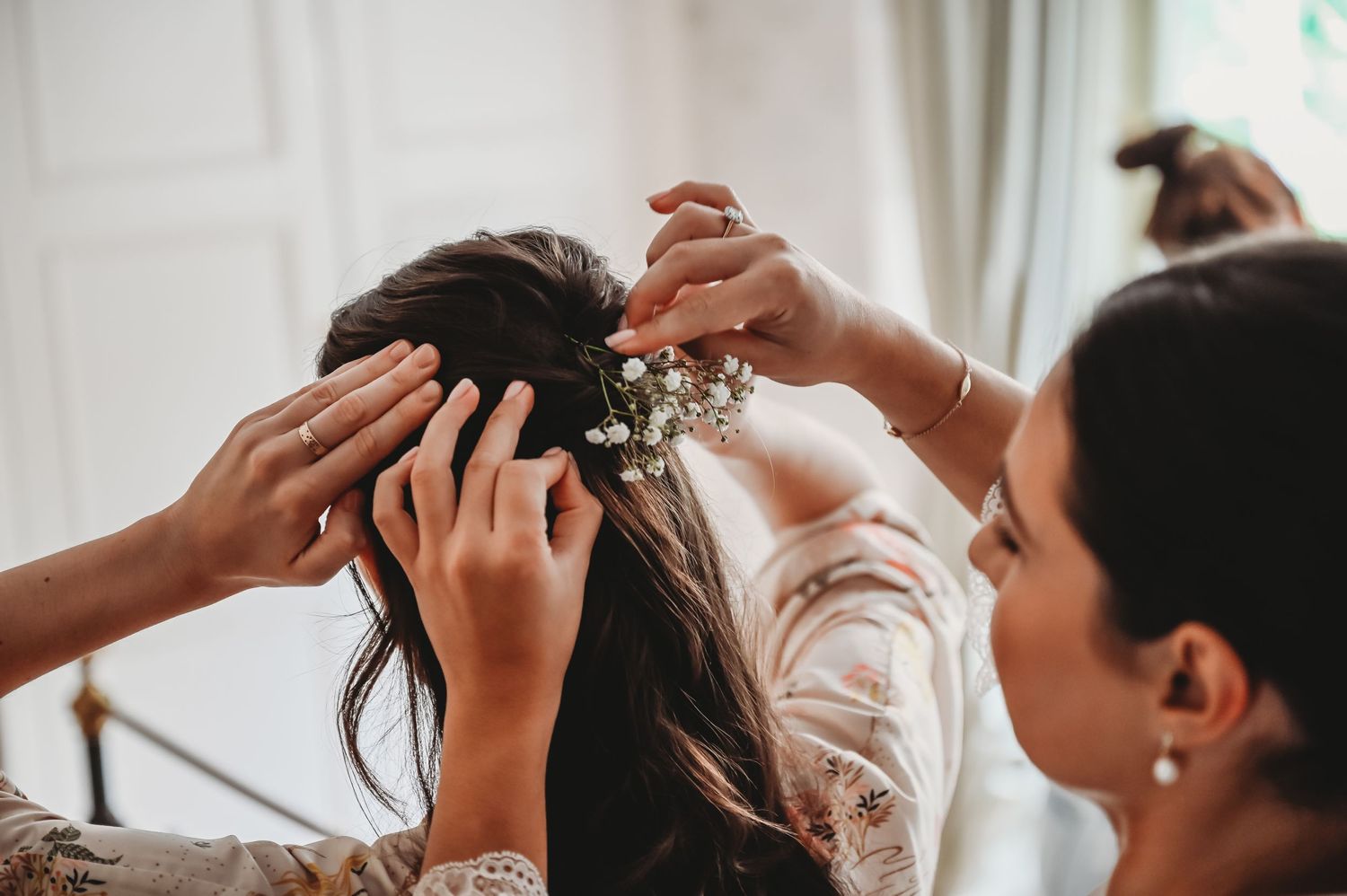 A delicate floral hair accessory being carefully placed into dark hair during wedding preparations.
