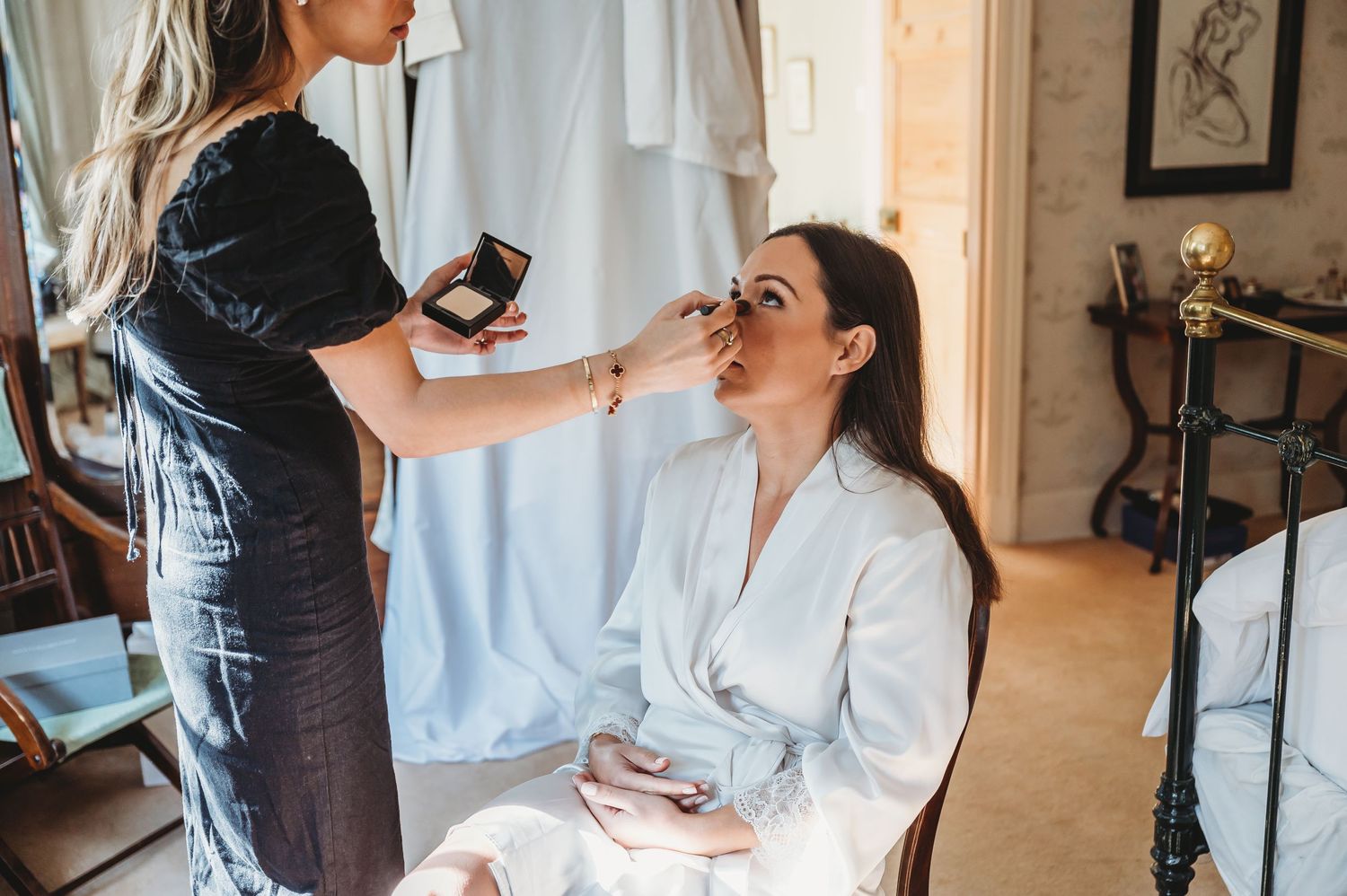 Makeup artist applying cosmetics to someone in a white robe during wedding day preparations.