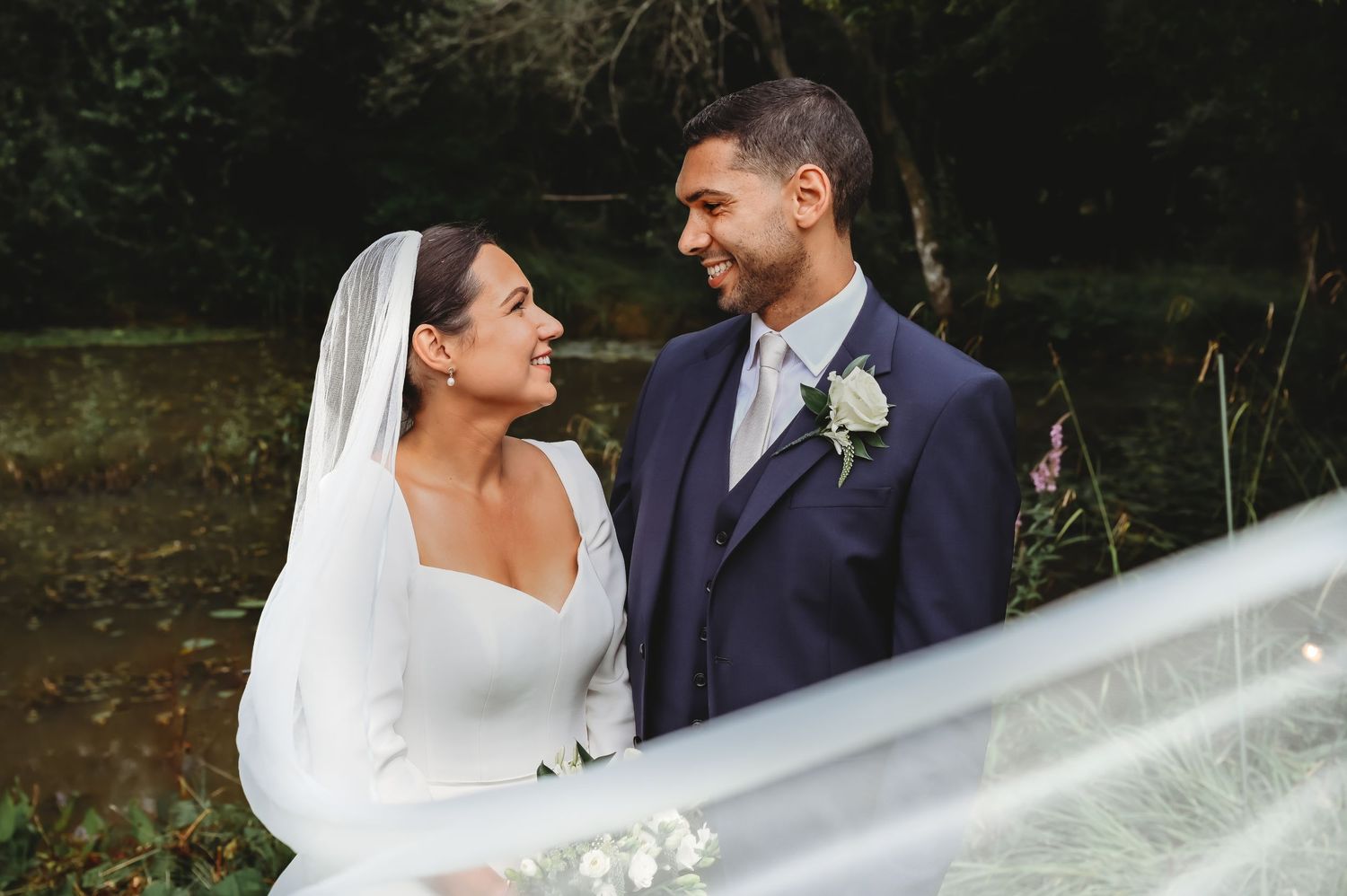 A joyful newlywed couple shares a moment together outdoors, with the bride's veil flowing in the breeze.