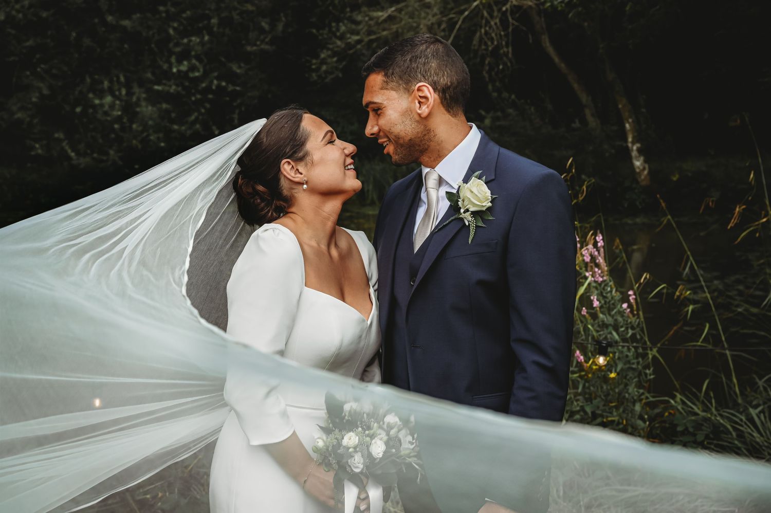 A joyful couple shares a romantic moment on their wedding day as the bride's veil flows in the breeze.