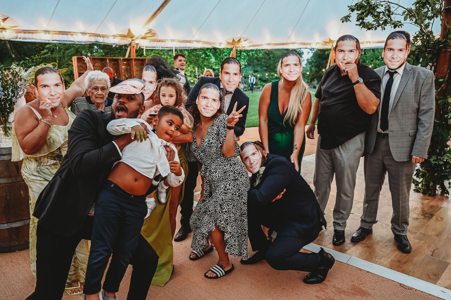 A lively group of wedding guests pose together under a tent at an outdoor celebration.