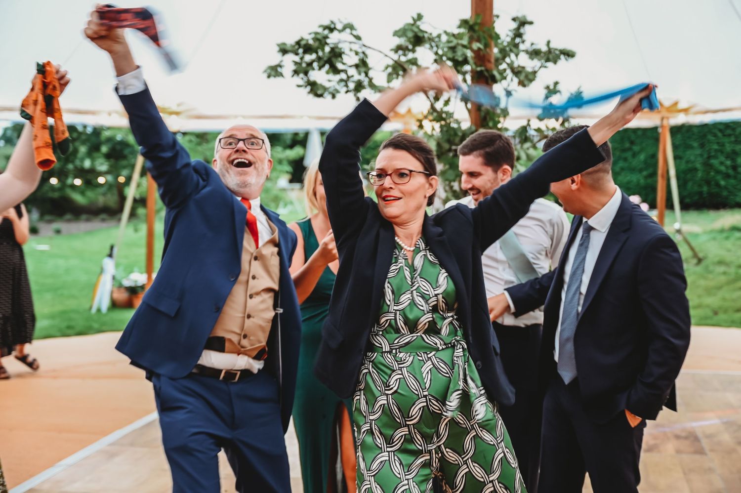 Wedding guests dance and celebrate joyfully on an outdoor dance floor at a daytime reception.