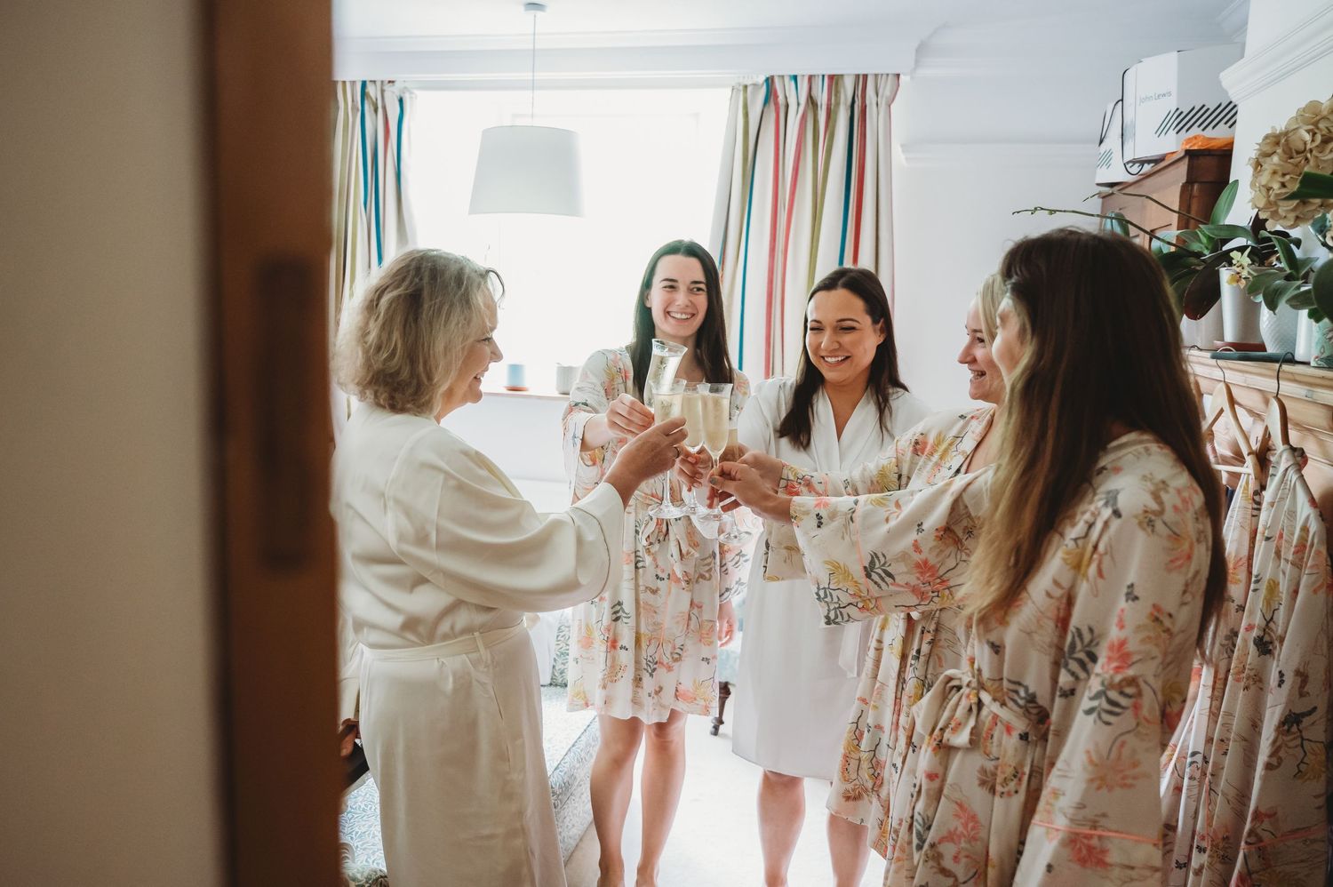 A group toasts with champagne while getting ready in floral robes during a wedding morning celebration.