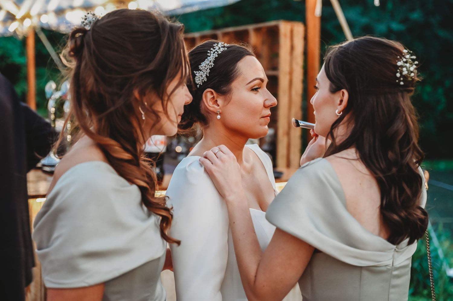 Three bridal party members in white wraps share an intimate moment during the wedding celebration.