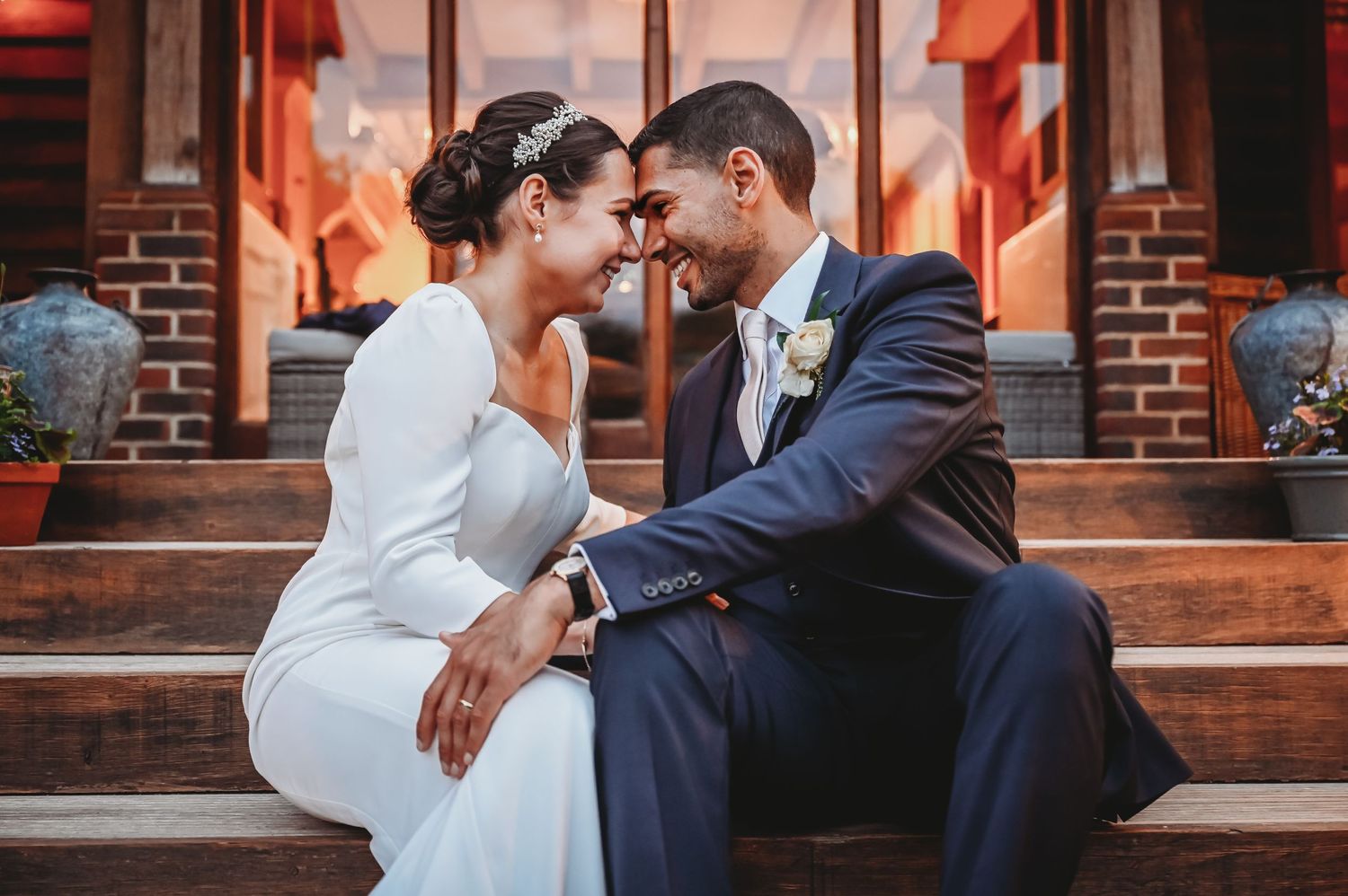 A romantic wedding couple shares an intimate moment while sitting on brick steps during sunset.