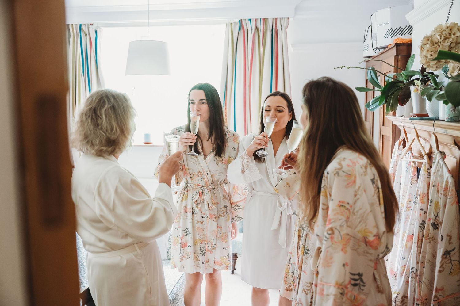 A group getting ready together in a bright room with floral dresses and champagne glasses.