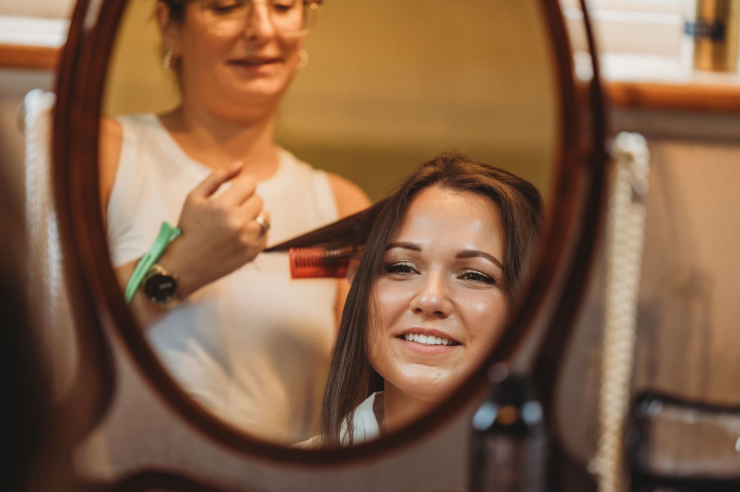 A reflection in a round mirror shows someone receiving a haircut at a salon.