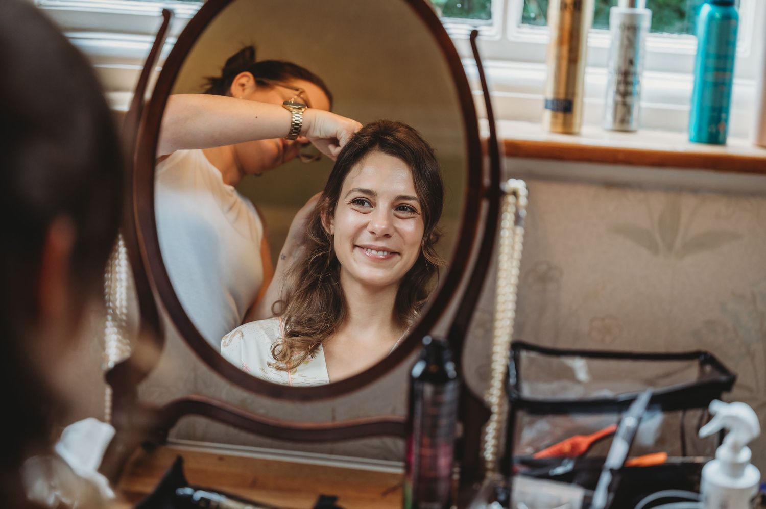 A reflection in a vanity mirror shows someone having their hair styled in a salon setting.